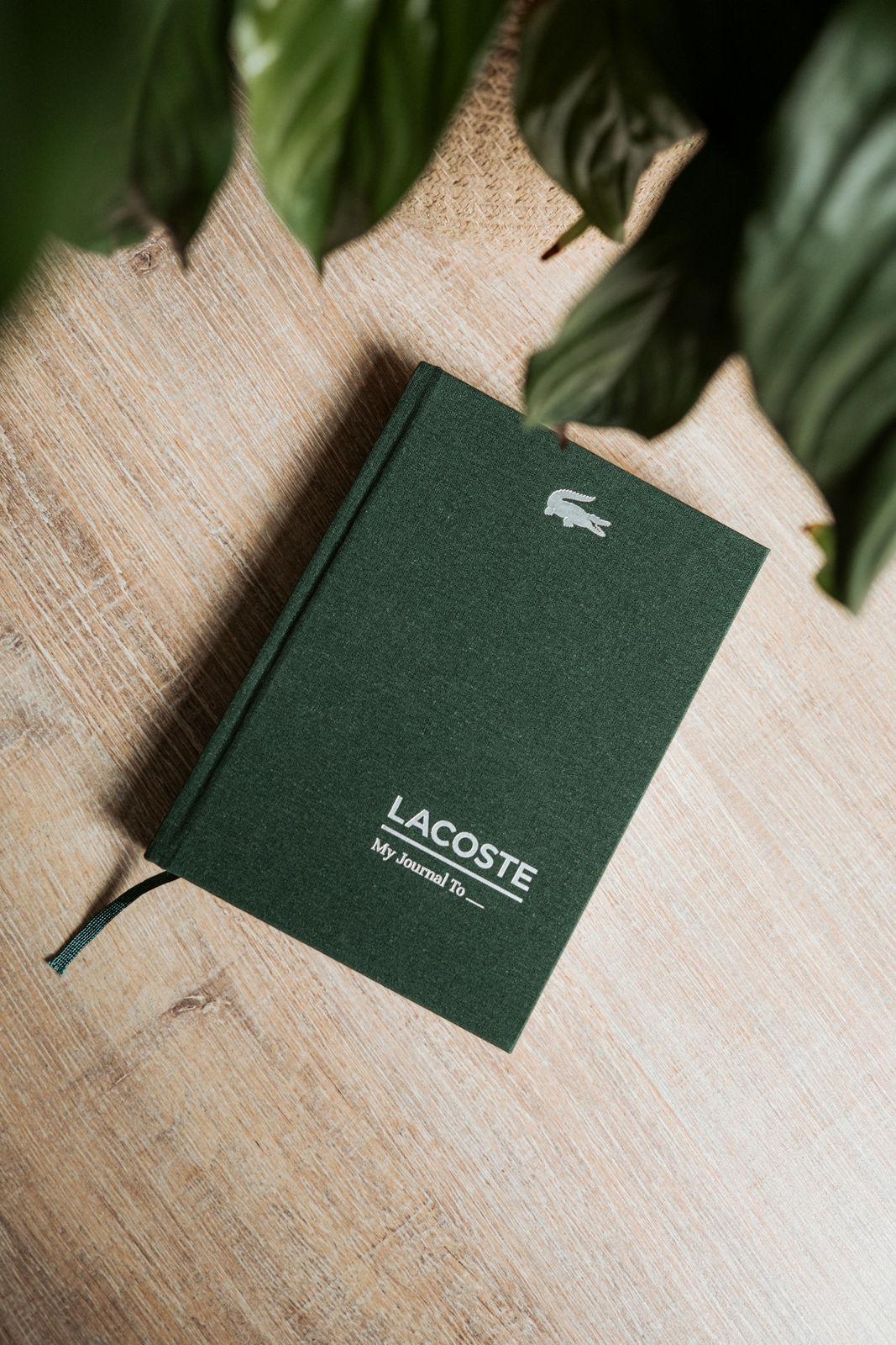 A linen-bound journal with the Lacoste crocodile crest, on a stone surface in morning light