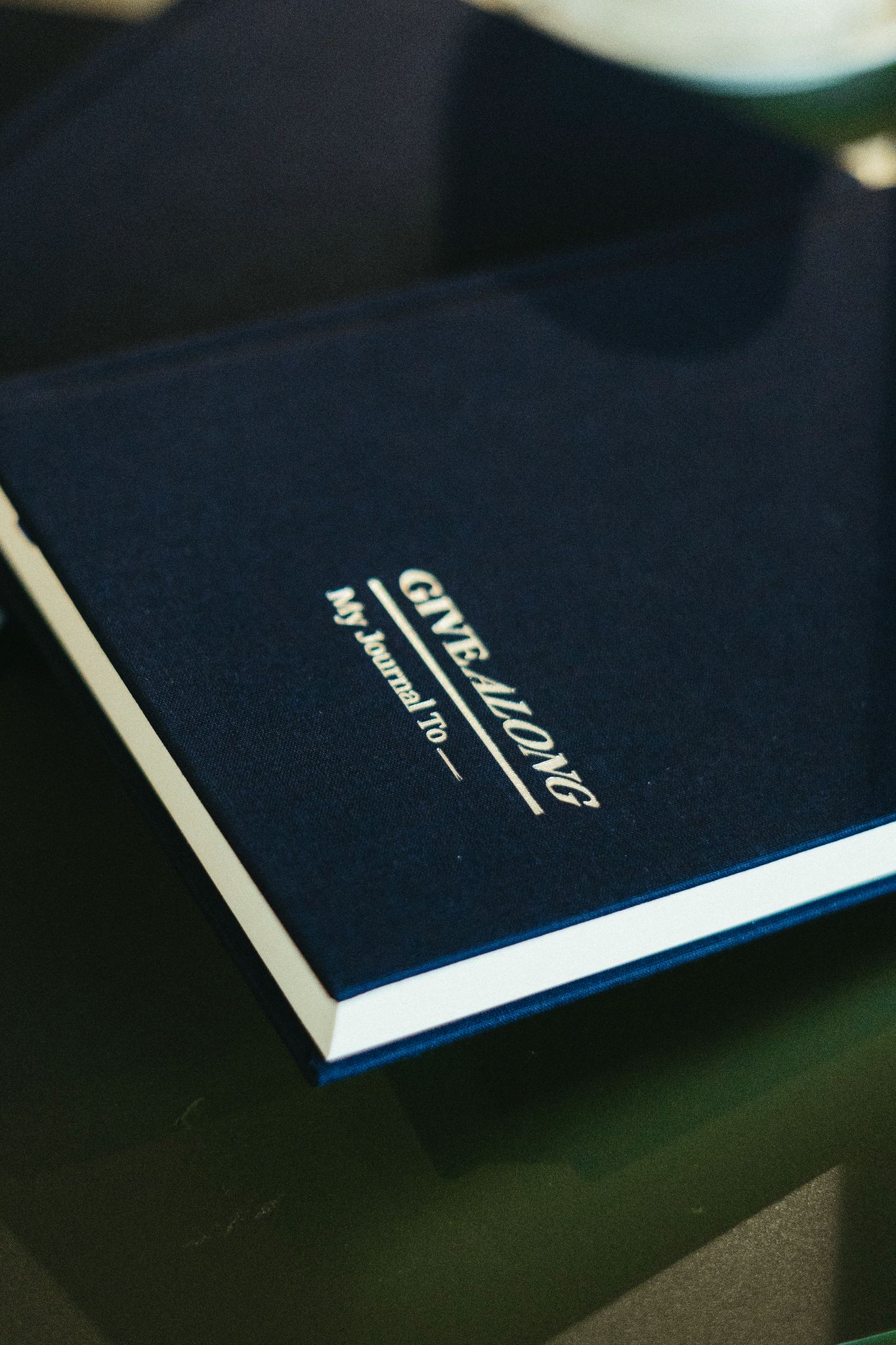 A linen-bound journal with foil-stamped logo on a stone surface
