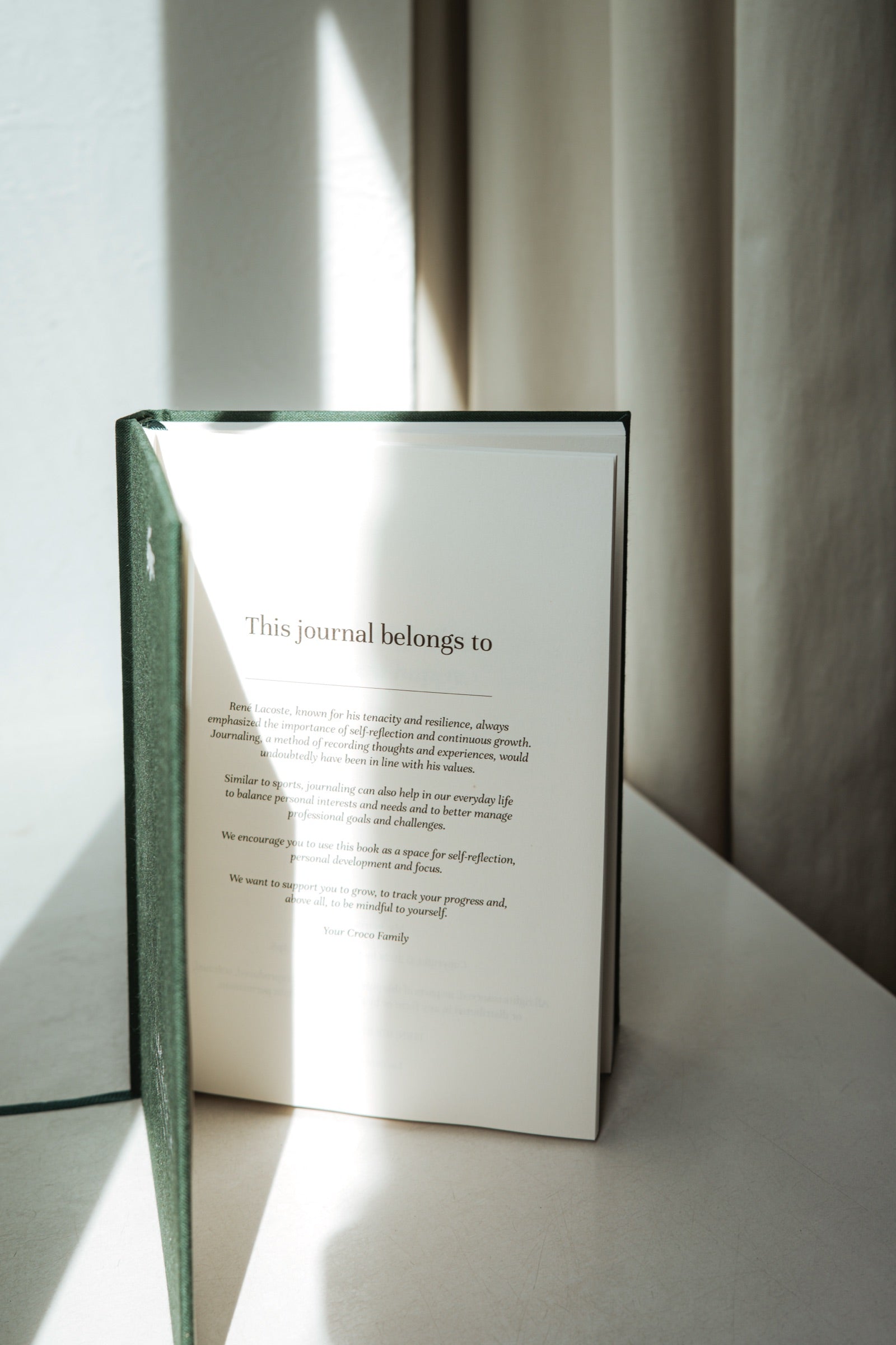 A Lacoste edition journal open to its custom interior dedication page, This journal belongs to, in soft window light