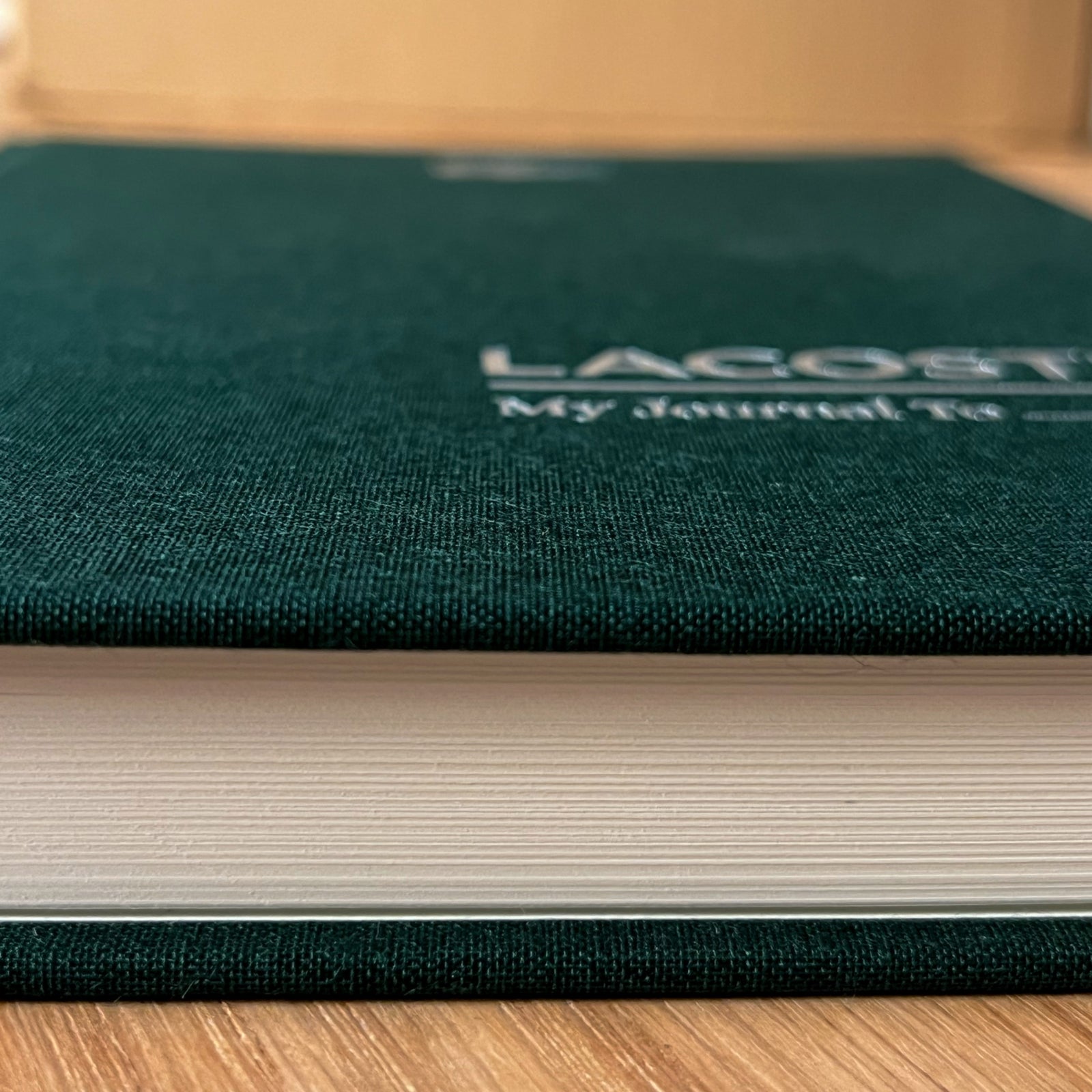 Close-up of the silver Lacoste embossing on the deep green linen cover of a co-branded journal